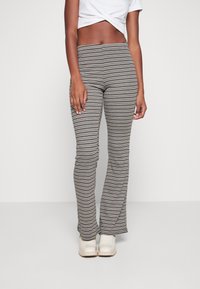 Pasiaste legginsy dzwonowate w kolorze czarnym, kremowym i taupe, z dopasowanym krojem i gładkim materiałem. Zestawione z jasnymi butami.