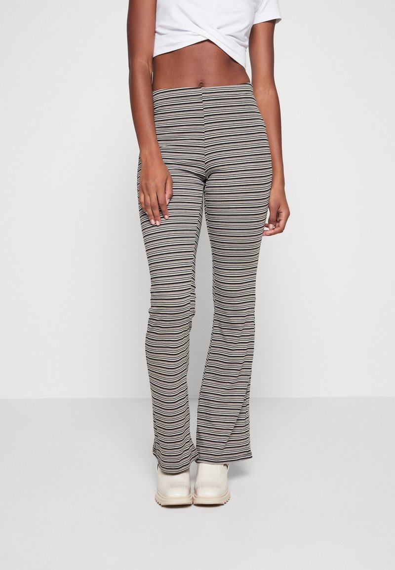 Pasiaste legginsy dzwonowate w kolorze czarnym, kremowym i taupe, z dopasowanym krojem i gładkim materiałem. Zestawione z jasnymi butami.