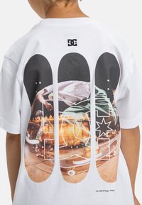 Camiseta blanca con un gran estampado gráfico en la parte posterior, que incluye visuales de skate con colores vibrantes y formas abstractas.
