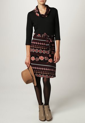 Svart långärmad topp, blommönstrad kjol med vinröda och flerfärgade ränder, beige hatt och beige ankelstövlar. Svarta strumpbyxor fullbordar outfiten.