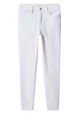 Person trägt eine schwarze Lederjacke, ein schwarz-weiß gestreiftes Shirt, weiße Skinny-Jeans und silberne Ballerinas und steht auf einem Betonboden.