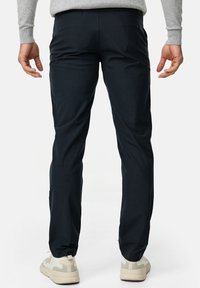 Hosen in Marineblau mit schlanker Passform, glatter Textur und minimalen Nähten, kombiniert mit hellen Sneakers.