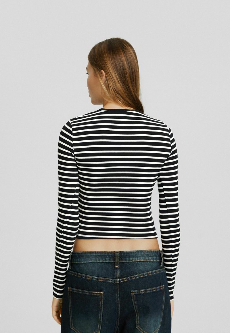 Schwarz-weiß gestreiftes Langarm-Crop-Top mit rundem Halsausschnitt, körperbetontem Schnitt und glatter Textur, kombiniert mit dunkelblauen, hoch geschnittenen Jeans.