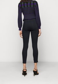 Černé legíny z denimu s viditelnými švy, nošené s pruhovaným svetrm v purpurové a černé barvě a černými sandály na podpatku.