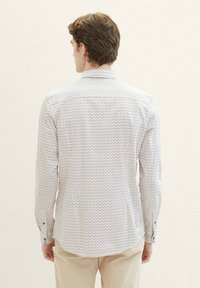 Witte langarmshirt met een geometrisch patroon in blauw, oranje en groen. Heeft een standaard kraag en knoopmanchetten, met een gebogen zoom.