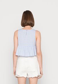 Top cropped em xadrez azul e branco com barra rodada, decote redondo e fecho de botão único nas costas; combinado com calções brancos desbotados.