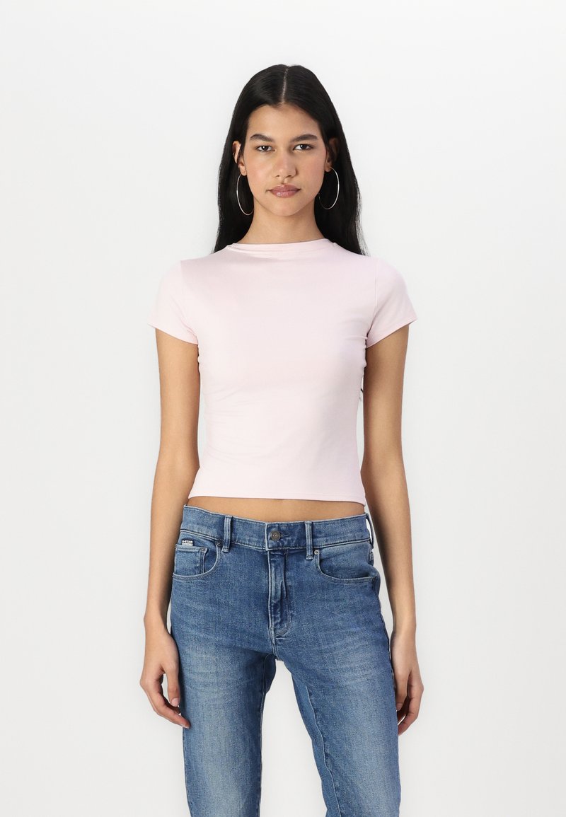 Lys rosa cropped t-skjorte laget av elastisk stoff, med rund hals og kortermede ermer, kombinert med blå denim jeans.