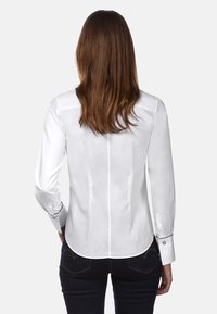 Witte fitted shirt met lange mouwen, gestructureerde rugnaden en knoopmanchetten. Glad textuur, afgeronde zoom, gedragen met donkere jeans.