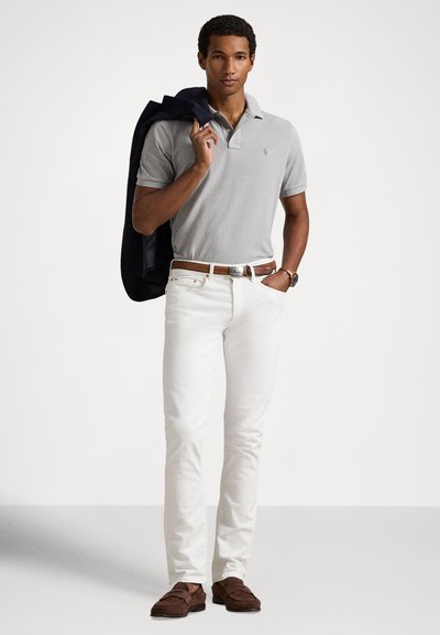 Γκρι πόλο πουκάμισο, λευκά τζιν στενής γραμμής, καφέ ζώνη και καφέ μοκασίνια. Σκούρο μπλε σακάκι περασμένο στον ώμο. Απλός, κλασικός σχεδιασμός.