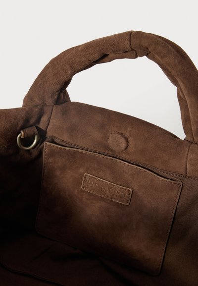 Pruunist nahast poe kott, mille sisepind on sile, sisaldab õmmeldud sildiga ning metallist rõngastega. Lihtne disain, ilma nähtavate mustriteta.