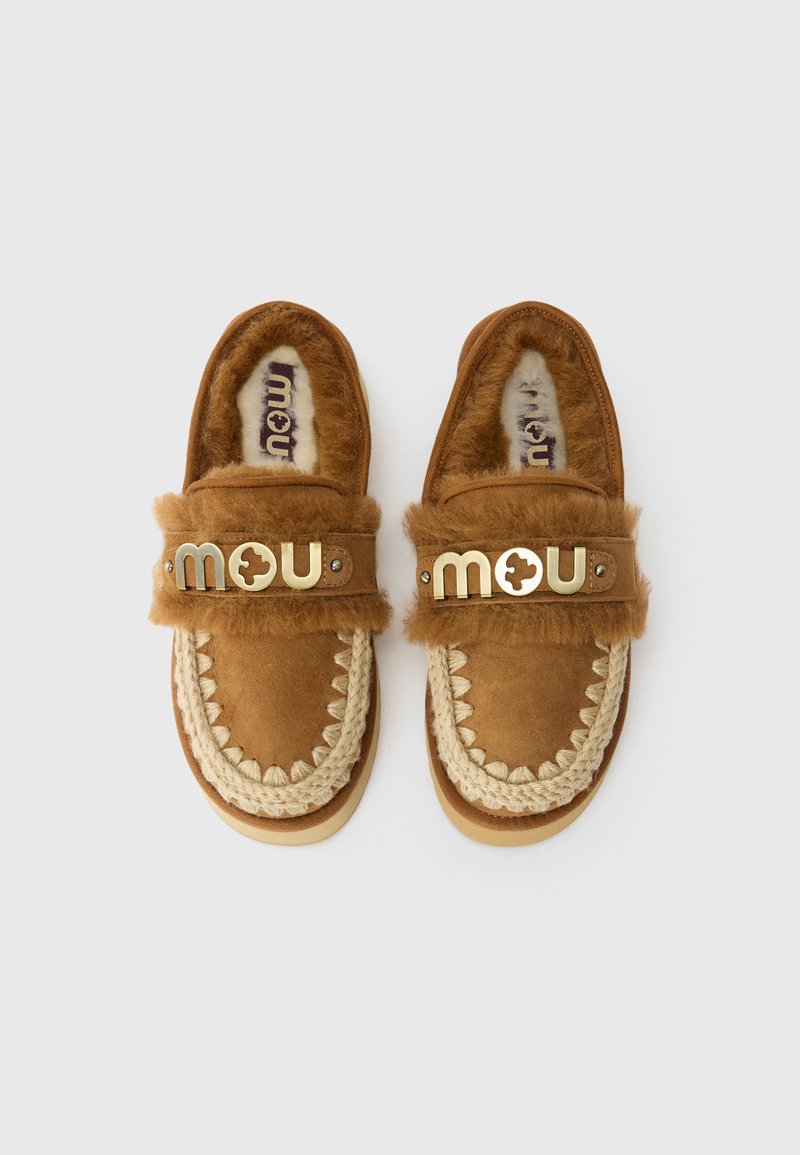 Para brązowych mokasynów zamszowych z futrzaną podszewką, plecioną lamówką i złotym logo "mou" na paskach, pokazana z góry na białym tle.