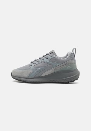 Szary niski sneaker Lacoste z teksturowanymi panelami, wiązaniem na sznurówki, grubą podeszwą i logo na pięcie oraz boku, pokazany z profilu.