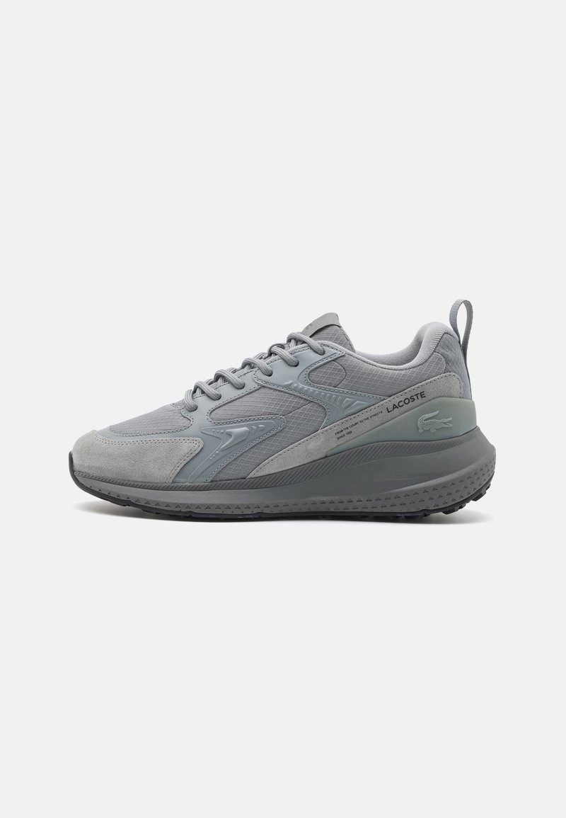 Baskets basses grises Lacoste avec des panneaux texturés, fermeture à lacets, semelle épaisse et logo au talon et sur le côté, montrées en profil latéral.