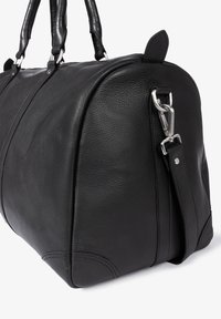 Schwarze Lederhandtasche mit rundem Design, strukturierter Oberfläche, zwei Griffen und abnehmbarem Schulterriemen mit silberner Beschläge.