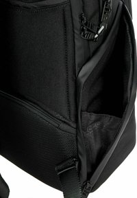 Interior de mochila negra con tela texturizada, compartimentos con cremallera y forro de patrón de panal. Correas ajustables y herrajes de plástico.