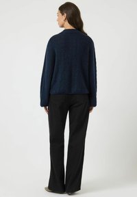 Maglione in maglia strutturata blu navy con maniche lunghe, vestibilità comoda e scollo rotondo, abbinato a pantaloni neri svasati.