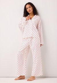 Hvid pyjamas sæt med rødt hjerte mønster; langærmet skjorte med knaplukning og løstsiddende bukser med brede ben; blødt, let stof.