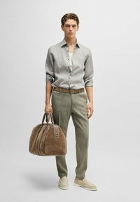 Camicia in lino grigia chiara con bottoni, canotta bianca, pantaloni in lino verdi, borsa in suede marrone con zip, scarpe slip-on neutre.