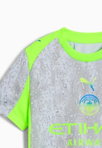Siva športna majica z teksturiranim vzorcem, ki spominja na kapljice, z svetlo zelenimi poudarki na ramenih in modrim logotipom Puma.