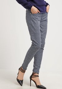 Pantalones ajustados en azul marino con un patrón floral blanco, que presentan un corte ceñido y bolsillos laterales. Combinados con zapatos de tacón negro.