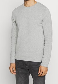 Szary sweter z okrągłym dekoltem wykonany z miękkiej tkaniny, z długimi rękawami, ściągaczami przy mankietach oraz standardowym krojem. Prosty i uniwersalny design.