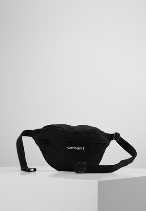 Sac banane Carhartt noir avec sangle ajustable et boucle en plastique posé sur une surface blanche sur un fond gris uni.