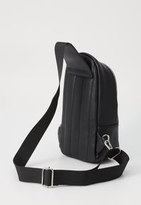 Black leather backpack with a vertical stripe design, adjustable black strap, and silver hardware. Slim profile with a zippered top.