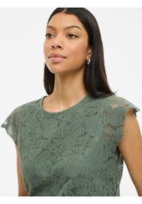 Groene kanttop met bloemenpatronen, korte fladdermouwen en een ronde halslijn. Textuurstof voegt diepte toe aan het ontwerp.