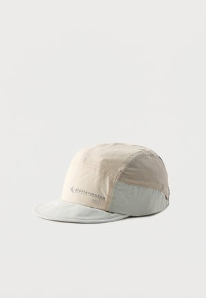 Casquette en tissu doux beige clair et gris avec une courte visière incurvée et le logo « Hüttenmusse SOL » sur le côté, présentée sur fond blanc uni.