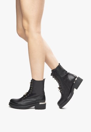 Black ankle boots made of synthetic leather, featuring metal eyelets, a front zipper, and a thick block heel with a silver accent.