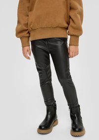 Zwarte faux leren legging met een gladde textuur en een slim fit, gecombineerd met een bruine oversized sweatshirt en zwarte enkellaarsjes met een tan kleurige zool.