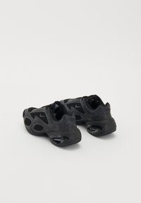 Chaussures de sport noires avec une tige en maille, un col rembourré, et un coussin d'air visible dans la semelle. Présentent une texture lisse et une forme unique.