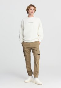 Felpa beige chiaro con una piccola scritta stampata, abbinata a pantaloni cargo color khaki con tasche laterali e completata da sneakers bianche.