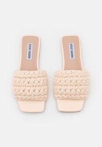 Sandali beige senza lace con una robusta tracolla intrecciata e una punta quadrata liscia. La suola è piatta e realizzata in un materiale di colore chiaro.