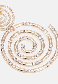 Accesorio en tono dorado en espiral con múltiples lazos, adornado con brillantes claros a lo largo de los bordes, que presenta una textura metálica suave.