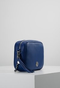 Borsa a tracolla blu in pelle con forma quadrata, hardware in argento e un dettaglio con frange. Presenta una chiusura con zip e un distintivo logo.