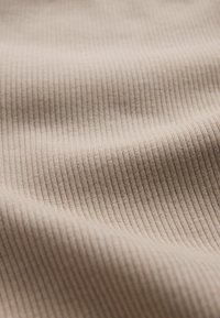 Close-up af beige ribbet stof, der viser fine lodrette linjer og bløde folder i materialet.