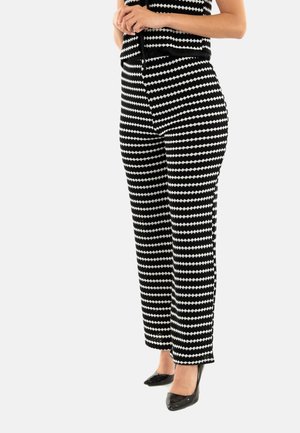 Top sin mangas de patrón en blanco y negro combinado con pantalones a rayas, con un diseño de diamantes y acentuado con tacones altos negros.