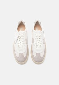 Sneakers brancos e cinza claro com materiais em camurça e couro, apresentando um bico redondo, design com atacadores e uma sola de borracha em contraste.