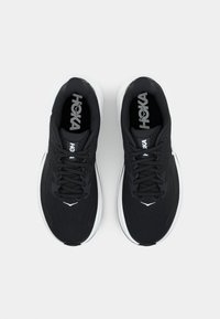 Chaussures de course noires avec une tige en mesh, semelle blanche et accents texturés. Présente des lacets et le logo de la marque sur la languette.