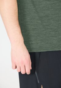 Vihreä teksturoitu urheilupaita lyhyillä hihoilla ja pieni "Nopea Kuiva" -logo helmassa, yhdistettynä mustiin urheilushortseihin.