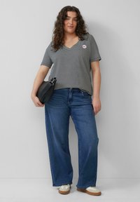 Gestreiftes kurzärmliges V-Ausschnitt-Shirt in Schwarz und Weiß, kombiniert mit lockeren blauen Jeans. Eine schwarze Schultertasche und weiße sowie beige Sneaker runden den Look ab.