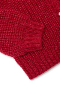 Gros plan sur une manche de pull en tricot rouge avec un poignet côtelé et un motif de points texturé sur fond blanc.