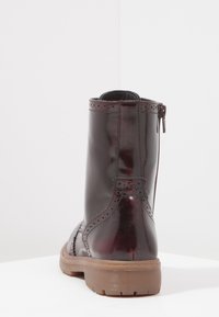 Botín de cuero burdeos oscuro hasta el tobillo con detalles de brogue, acabado suave, cremallera lateral y suela de goma gruesa.