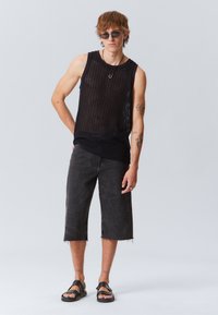 Top noir sans manches en tricot côtelé avec une coupe décontractée. Porté avec un short en denim noir raccourci présentant un ourlet en déchirure et une finition texturée. Sandales noires.