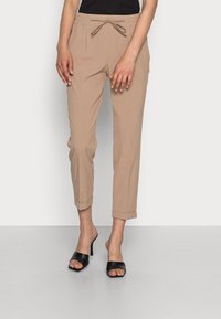 Pantaloni cropped beige con vita elastica e dettaglio del nodo, dotati di due tasche laterali e risvolti. Indossati con mule neri da infilare.