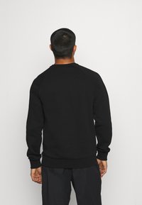 Sudadera negra con cuello redondo y mangas raglán. Presenta una textura suave y dobladillo acanalado. Llevada con pantalones oscuros, mostrando un diseño sencillo.