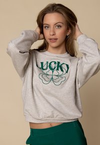 Lichtgrijze cropped sweatshirt met "LUCKY" geborduurd in donkergroen en een klavertje vier ontwerp. Bevat lange mouwen en een afgeronde zoom.