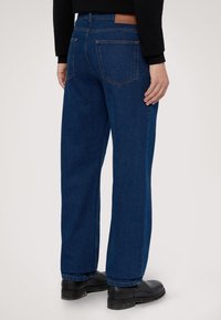 Modré denimové džíny se střihy rovného nohu, s koženou nášivkou na zadním pase, dvojitým švem a zadními kapsami.