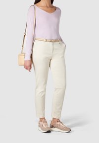 Haut violet clair à manches longues, pantalon beige ceinturé, et baskets beiges avec des accents texturés. Petit sac bandoulière beige.